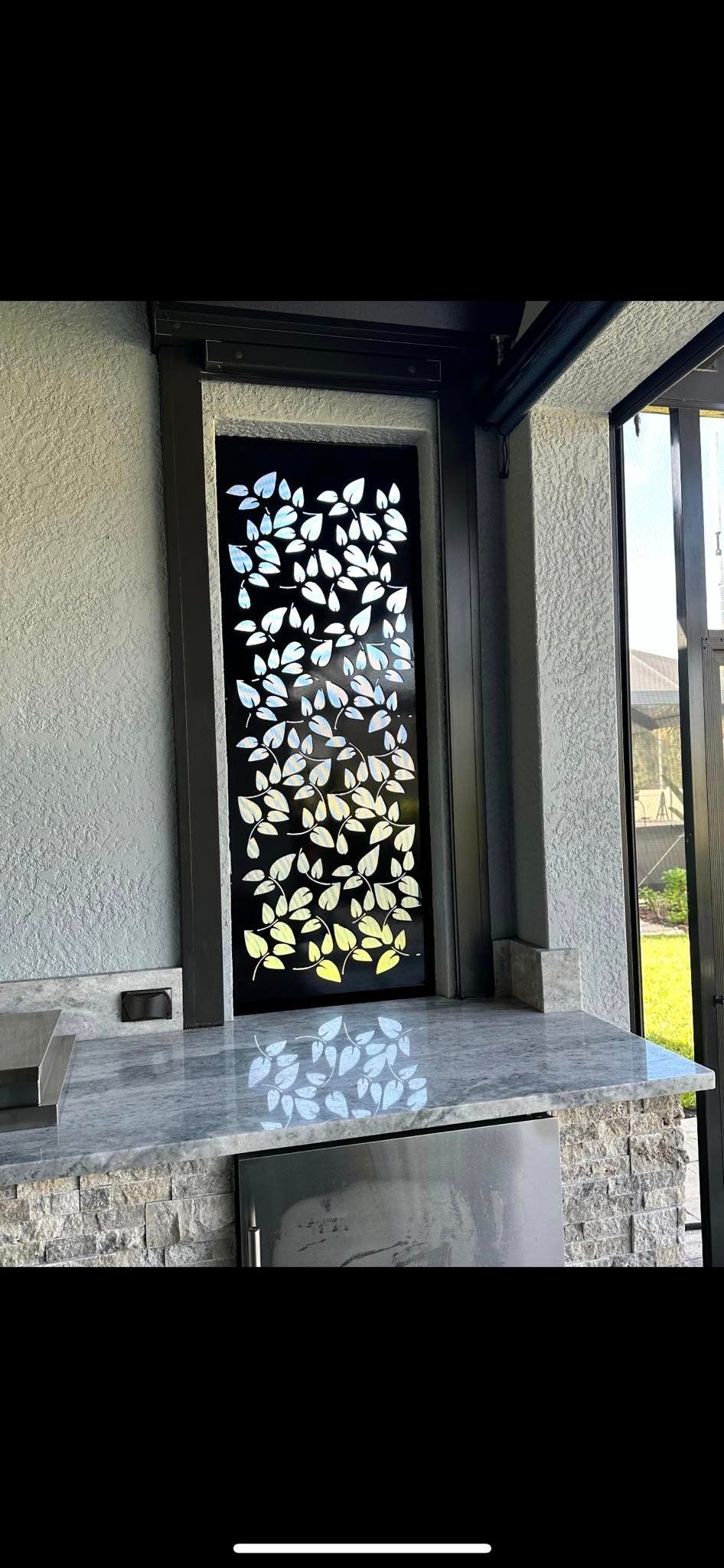Outdoor kitchen with granite countertop, leaf-patterned metal screen, and stone facade.