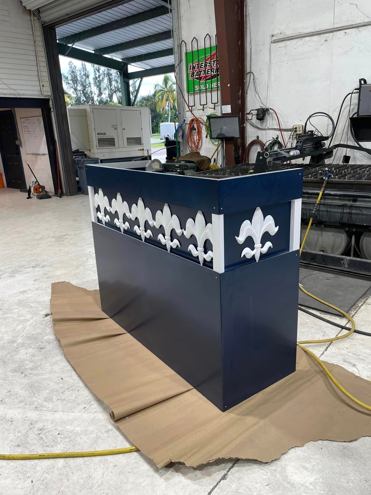 A navy blue and white fleur-de-lis cabinet in a workshop with equipment and open garage door.