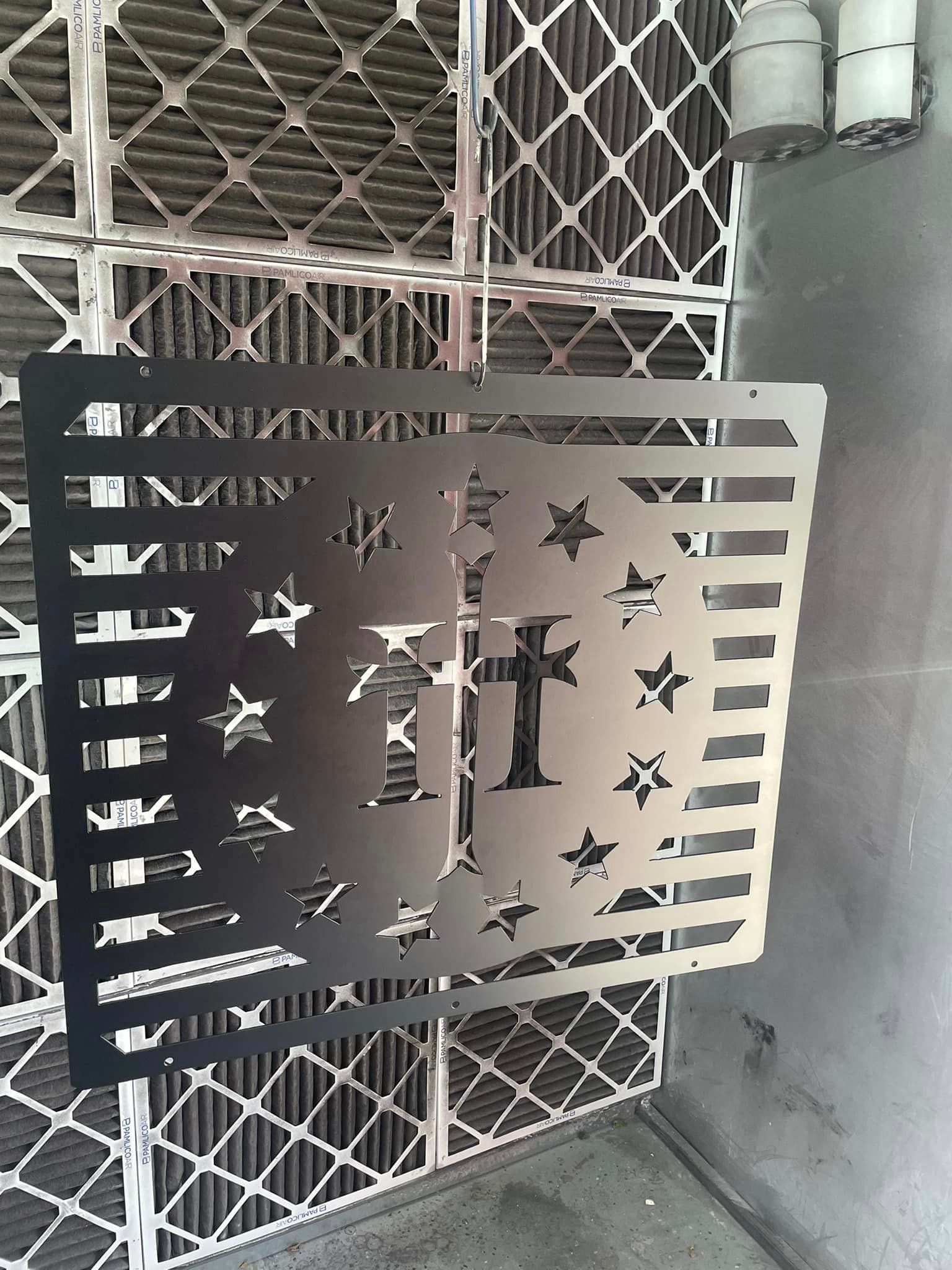 Metal cut-out of a flag with a cross and stars, in front of air filters.
