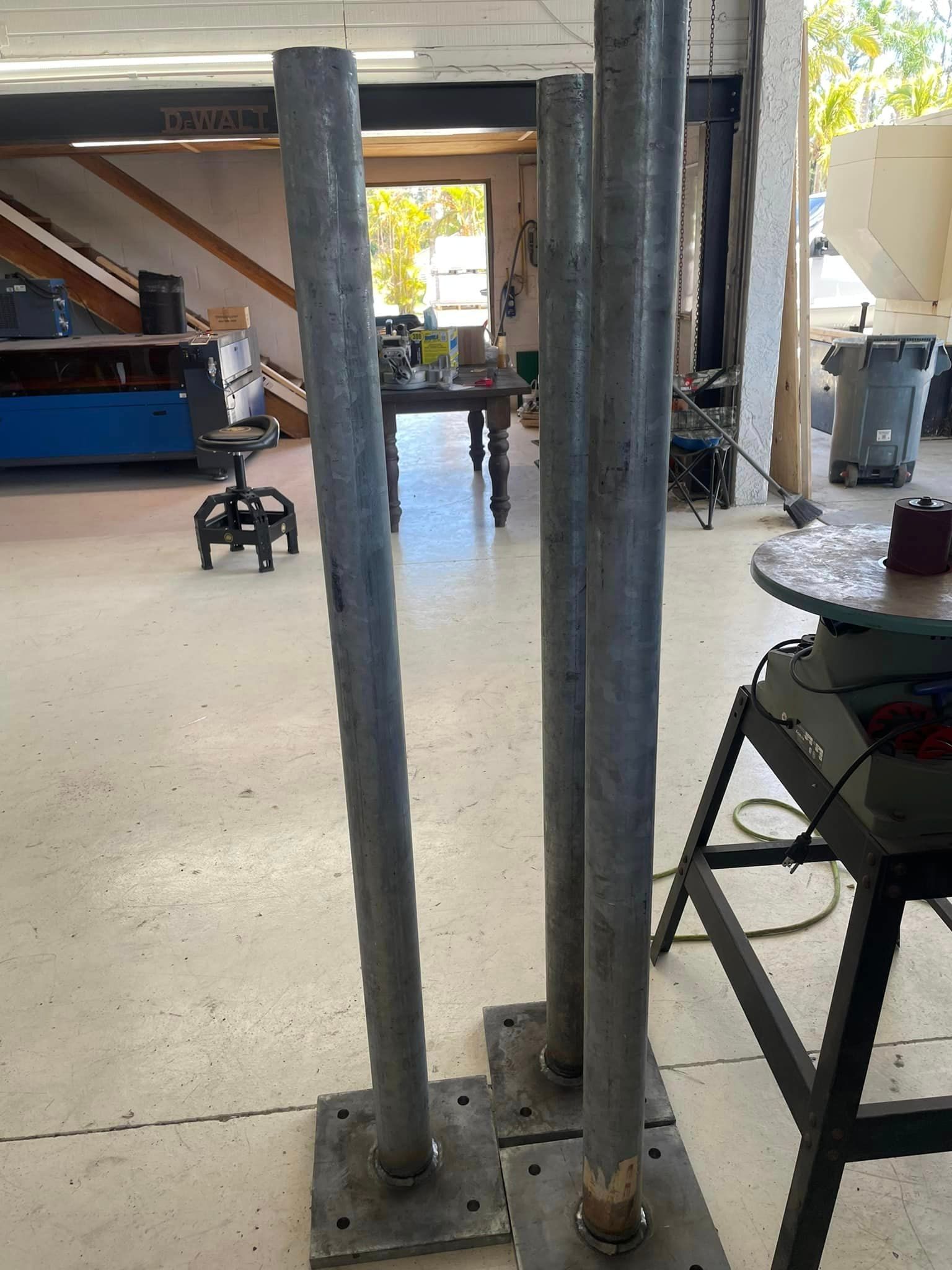 Four metal poles welded to square bases, standing in a workshop.