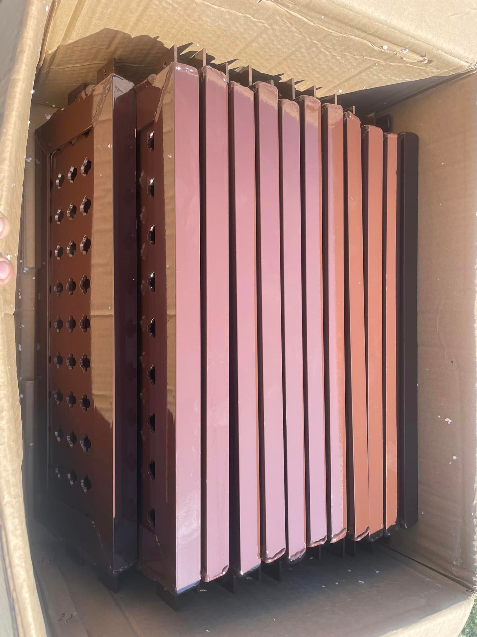 Brown metal panels stacked inside a cardboard box, presumably for assembly.