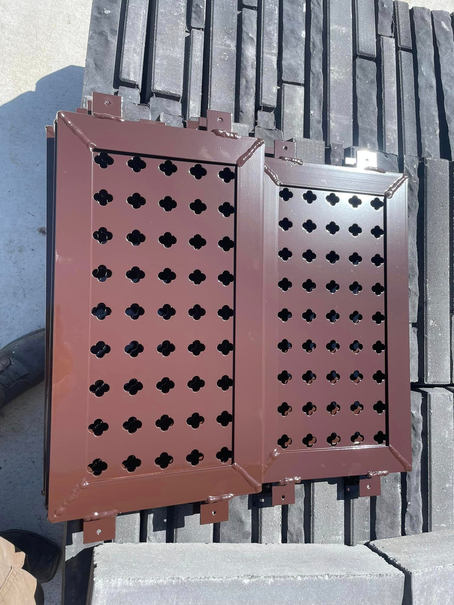 Two brown metal vent covers with decorative cutouts, resting on gray pavers.