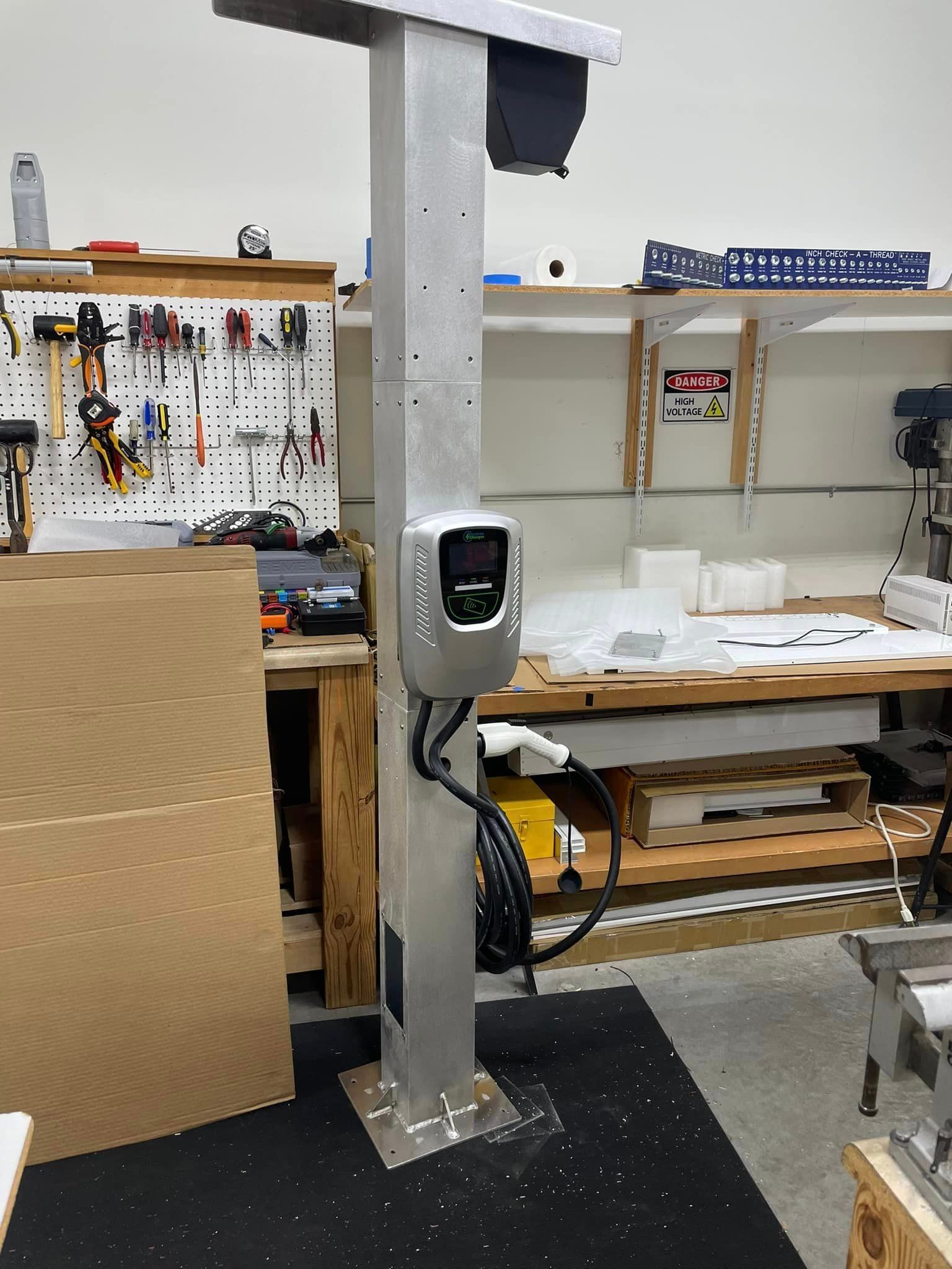 Electric vehicle charger station, silver, mounted on a post in a workshop.