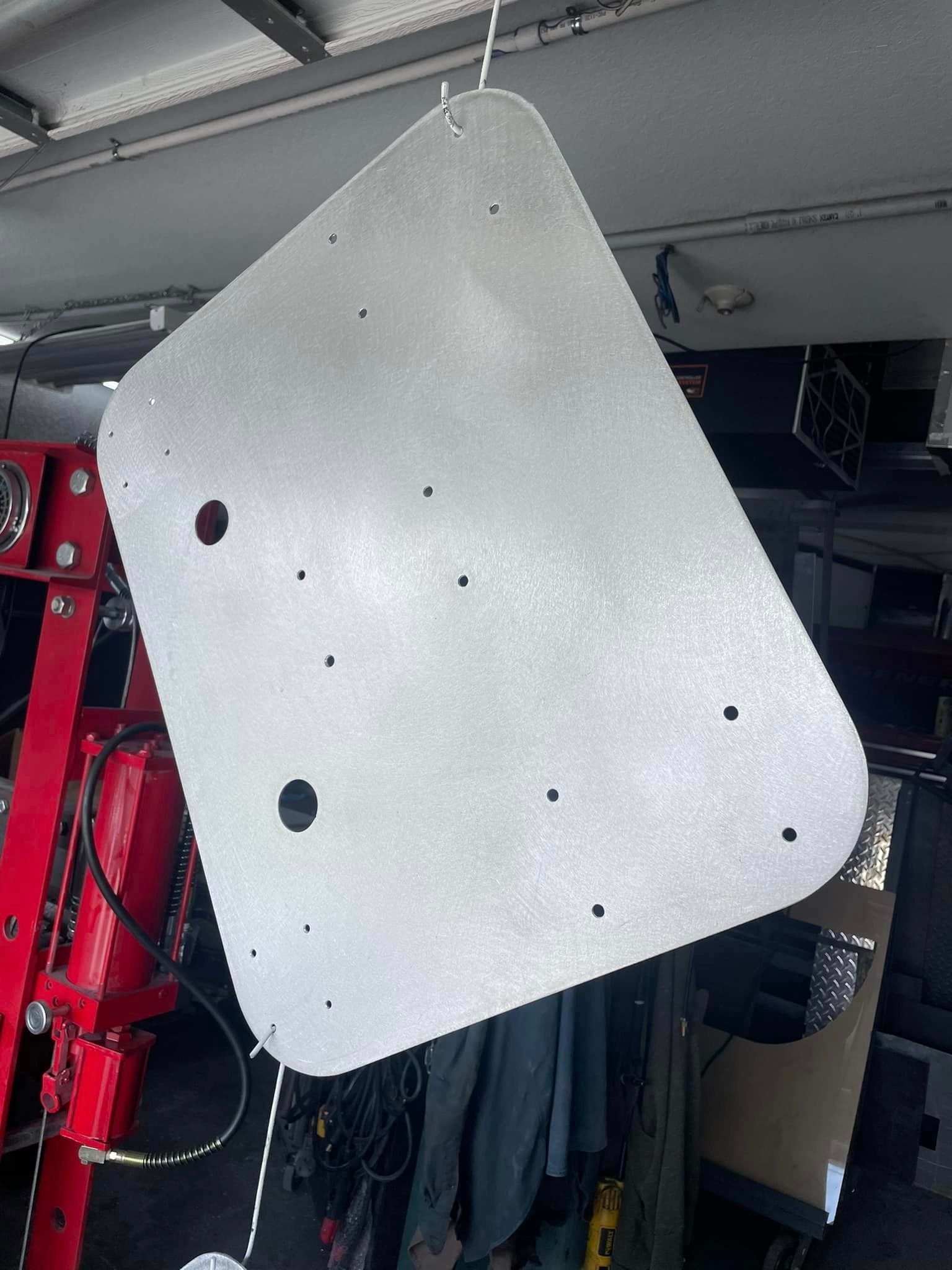 A freshly painted, light gray metal panel with several holes, hanging in a garage setting.