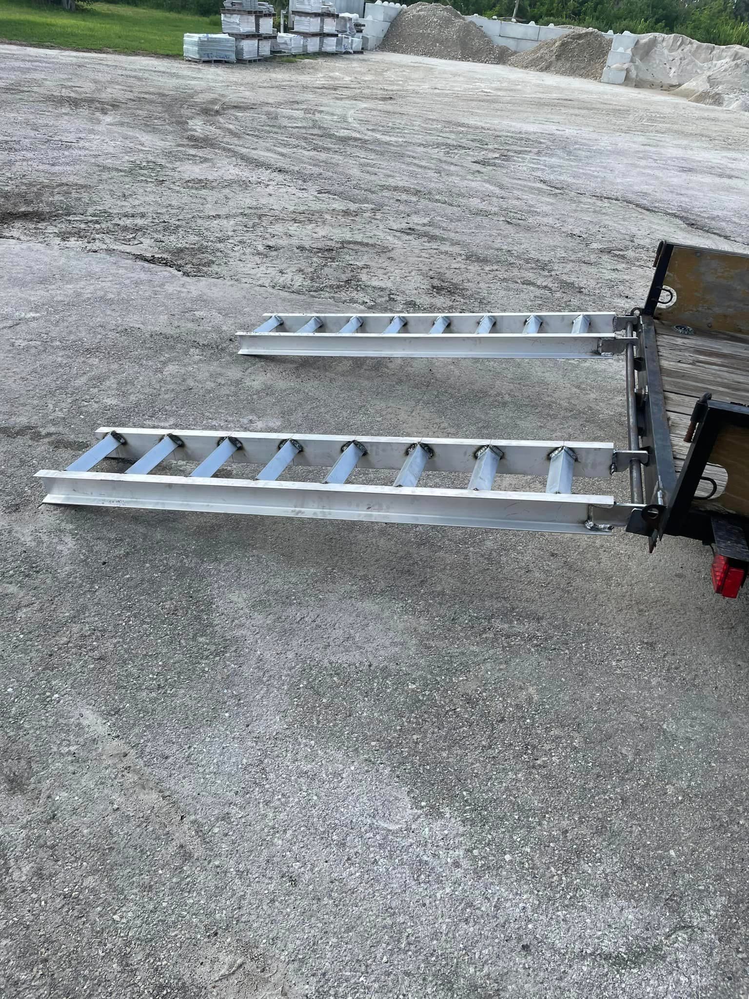 Two aluminum ramps extend from the back of a utility trailer on a concrete surface.