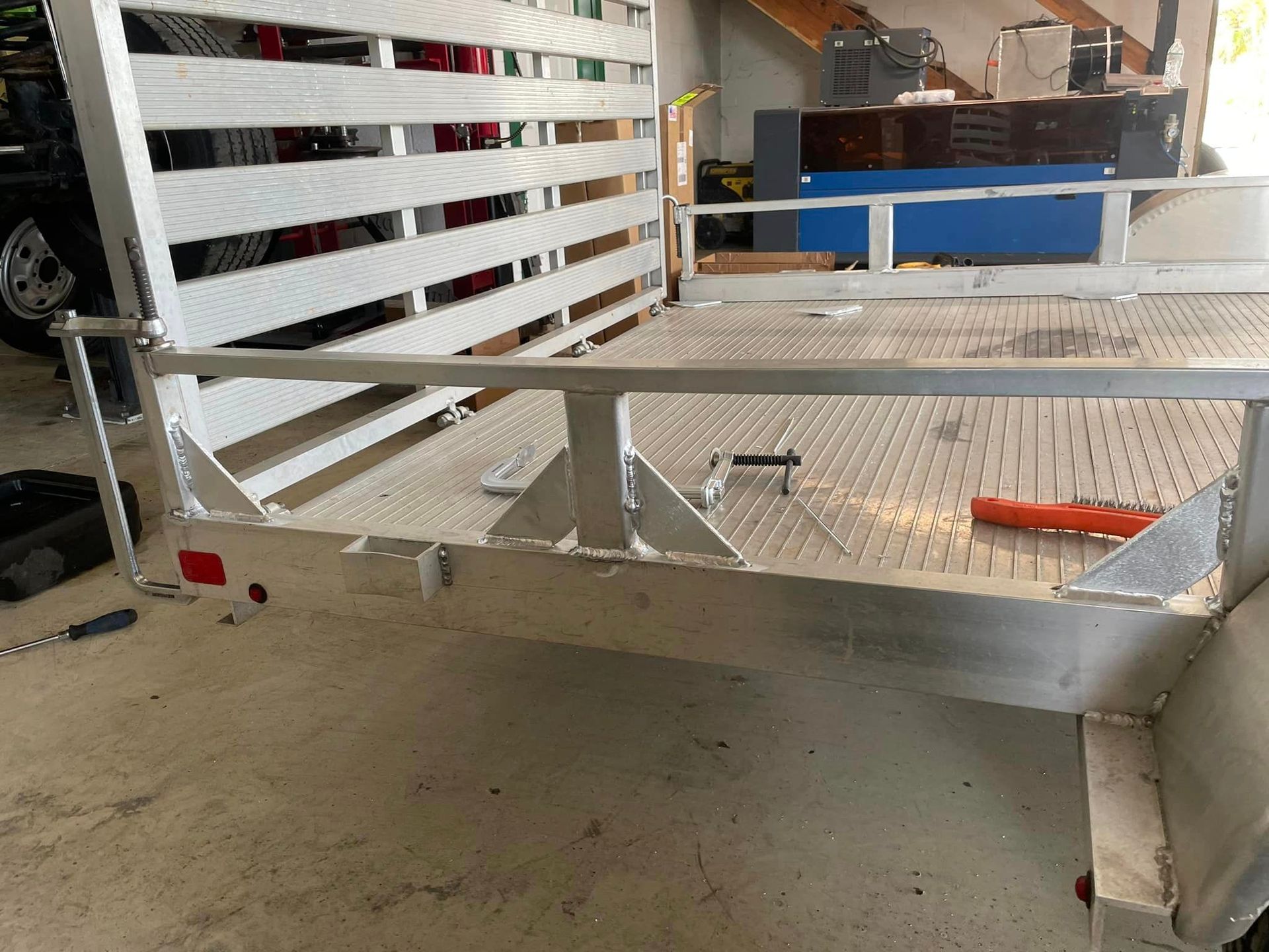 Aluminum trailer bed with side rails and rear lights in a garage.