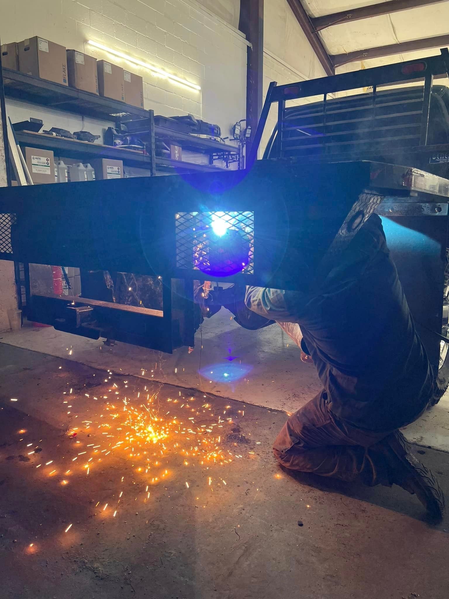 Person welding on a black metal structure, sparks flying in a workshop.