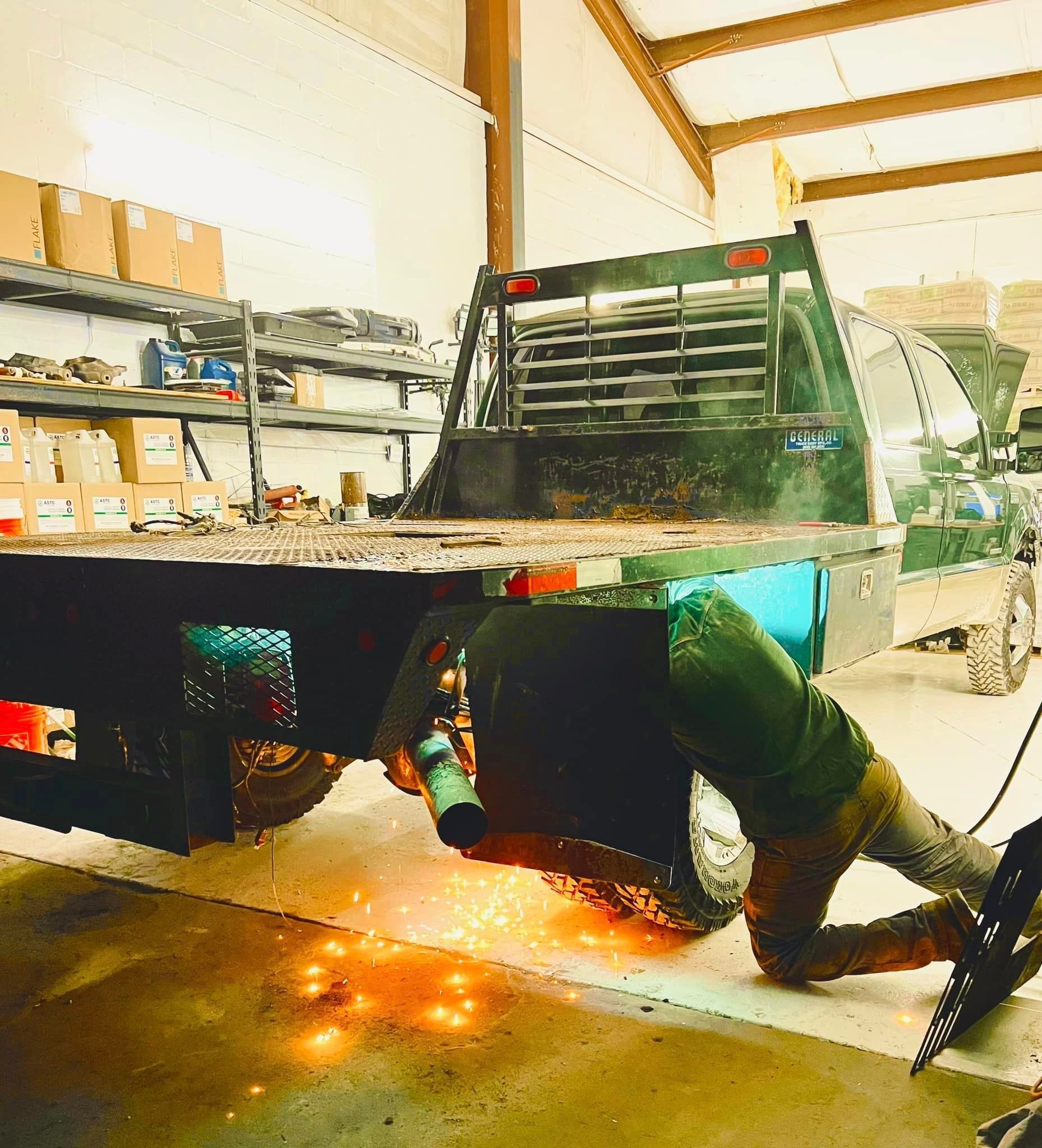 A person welding on the rear of a flatbed truck in a shop; sparks fly.