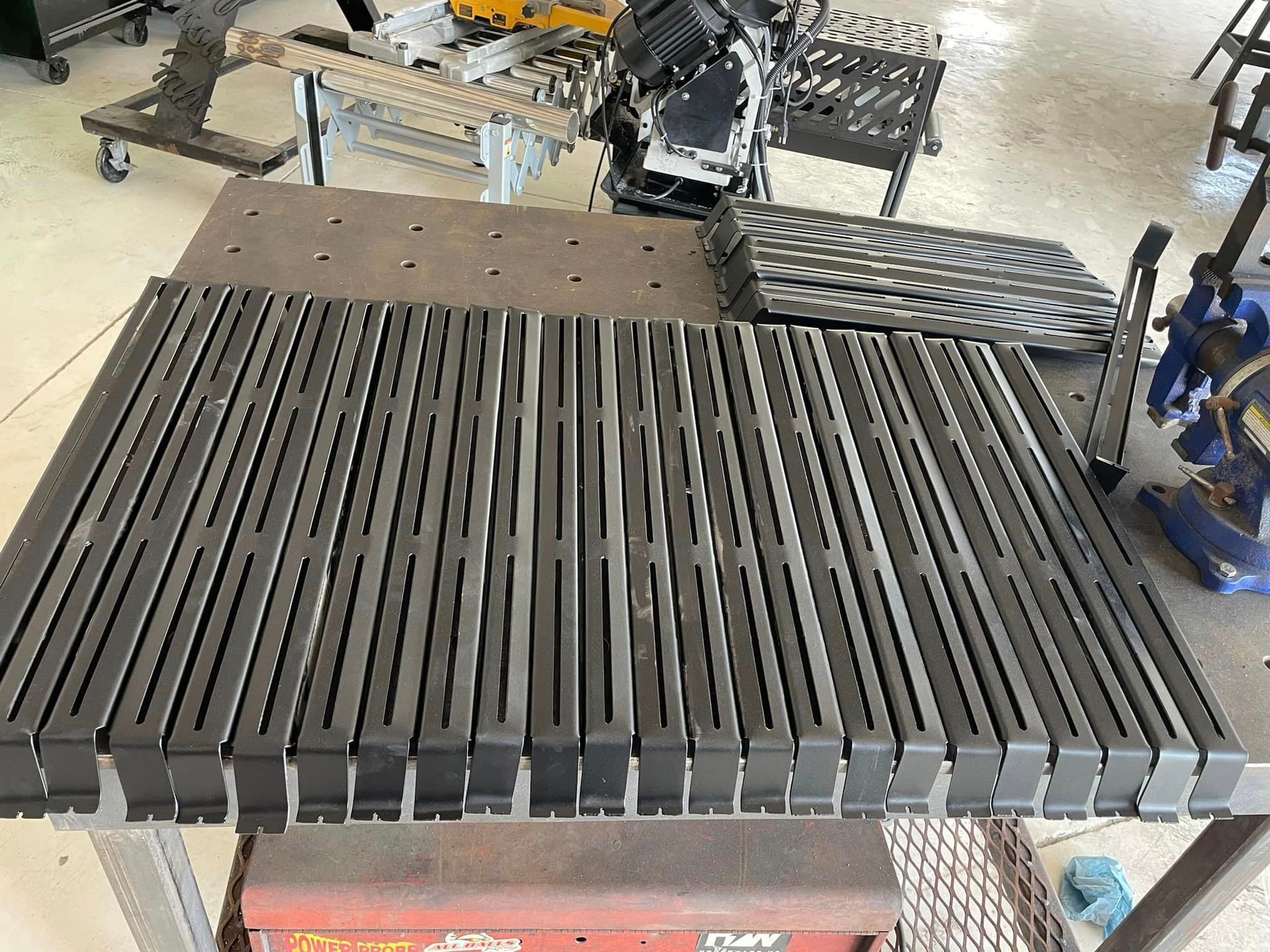 Metal fabrication: Rows of slotted metal pieces on a work table in a workshop setting.