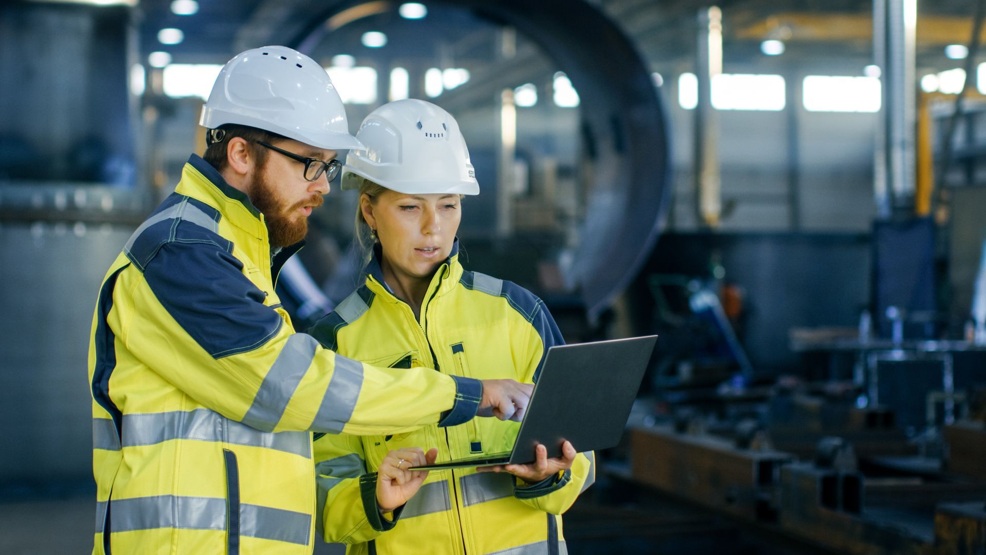A man and a woman are looking at a laptop in a factory.