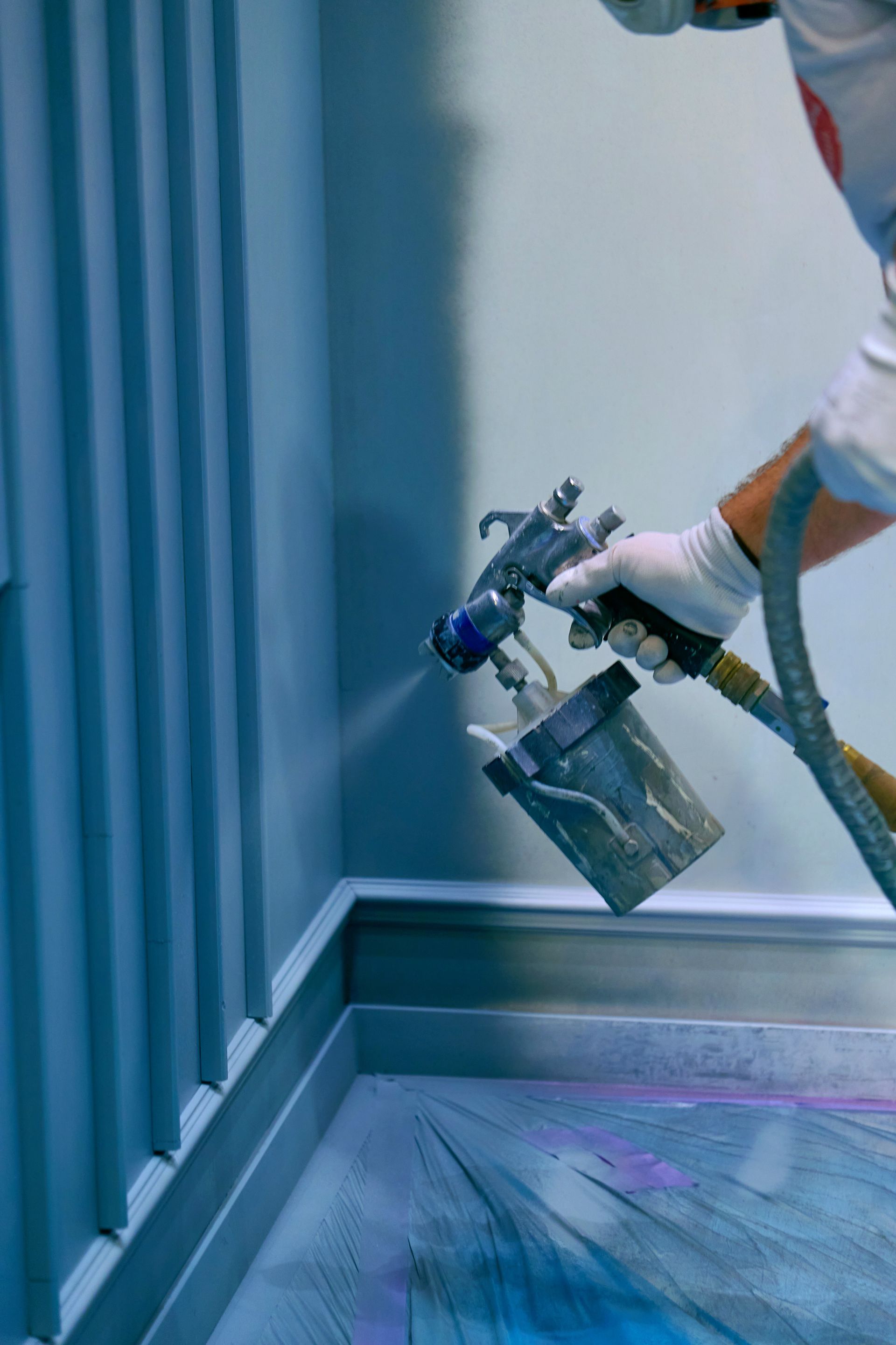 Worker spray-painting a metal surface in a blue industrial booth