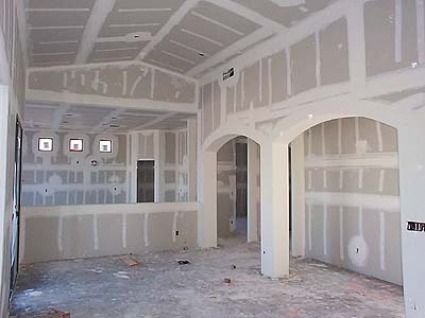 Empty drywall interior of an unfinished room with arched openings and exposed ceiling beams