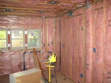Unfinished room with pink insulation, exposed ceiling joists, and windows along the back wall.