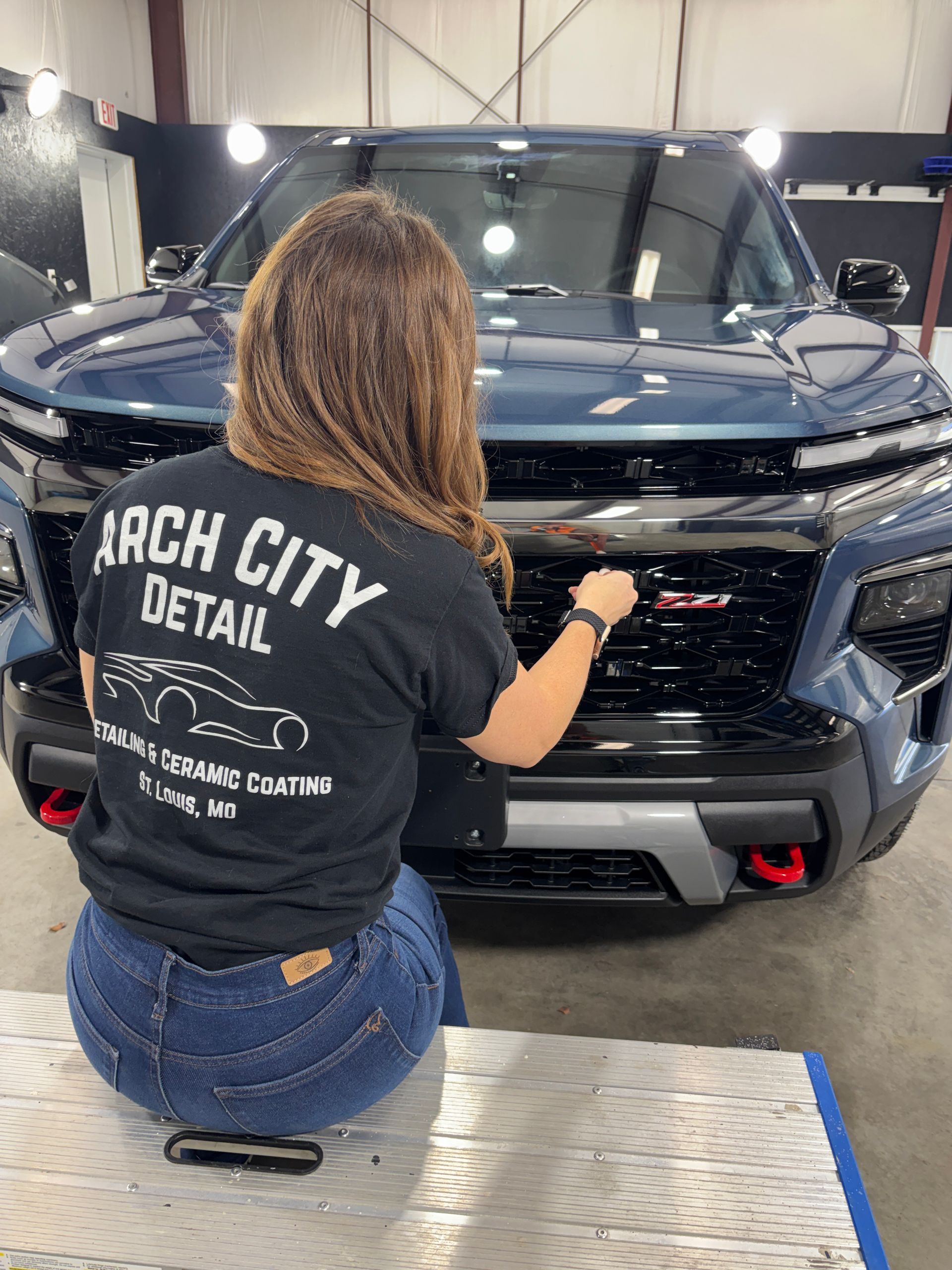 Black-gloved hand applying ceramic coating to red car's hood, near headlight.