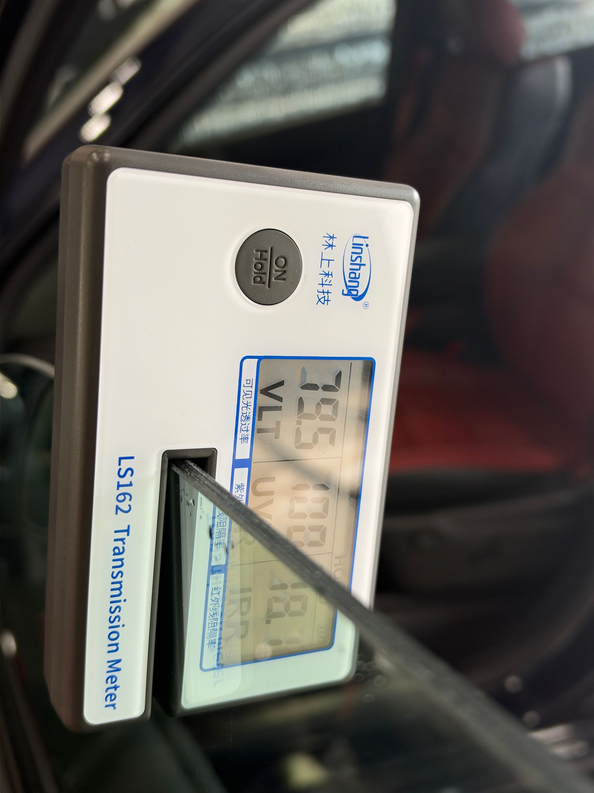 Tint meter measuring visible light transmission through a vehicle’s front side window.