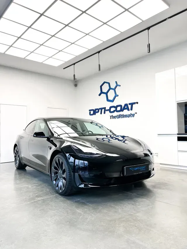 Black sedan in a bright auto detailing studio with a “SPT-COAT” wall logo.