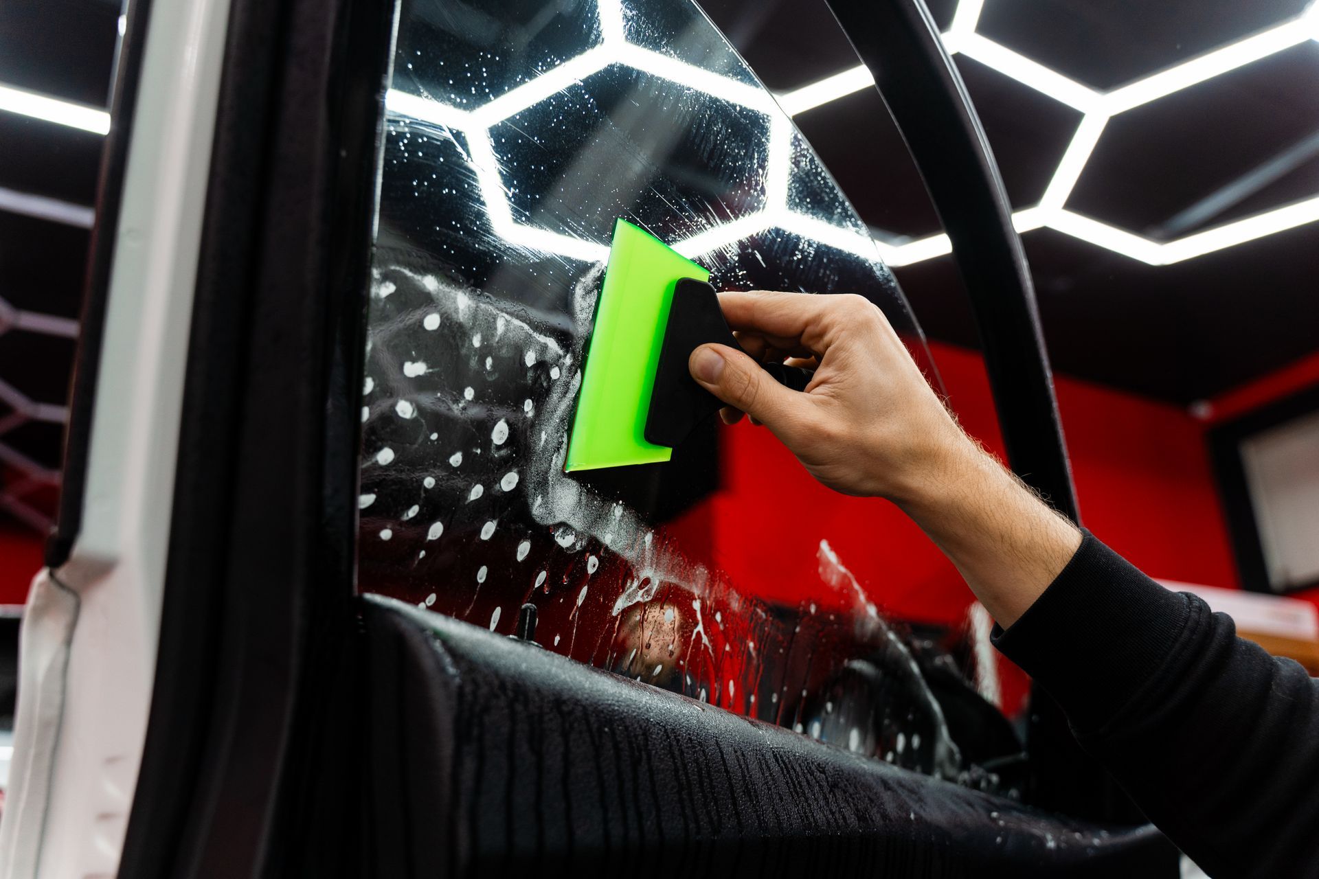 Hand cleaning a car window with a green squeegee, water droplets visible on the glass
