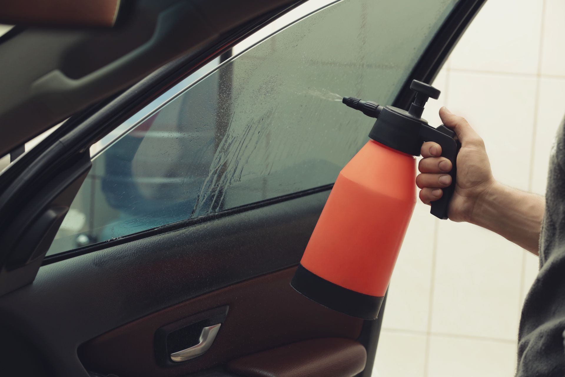 Person spraying orange cleaner on a car window with a handheld sprayer