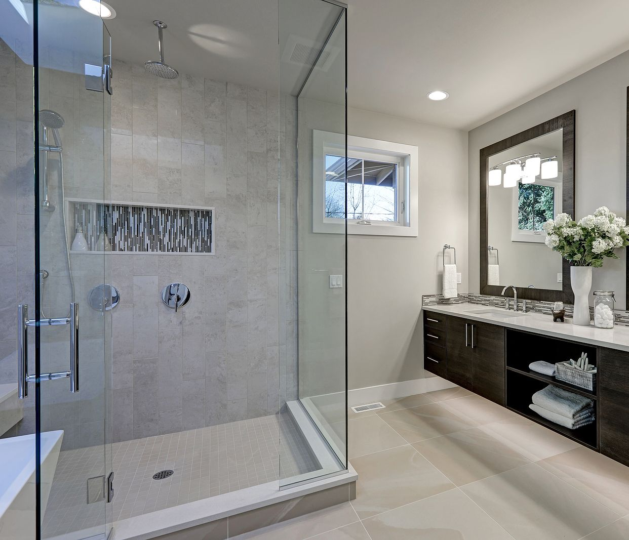 Modern bathroom with a glass-enclosed shower, dark wood vanity, and a window.