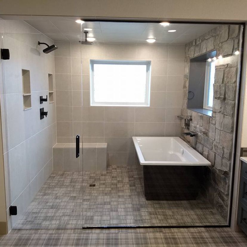Modern bathroom with walk-in shower, bathtub, and stone accent wall.
