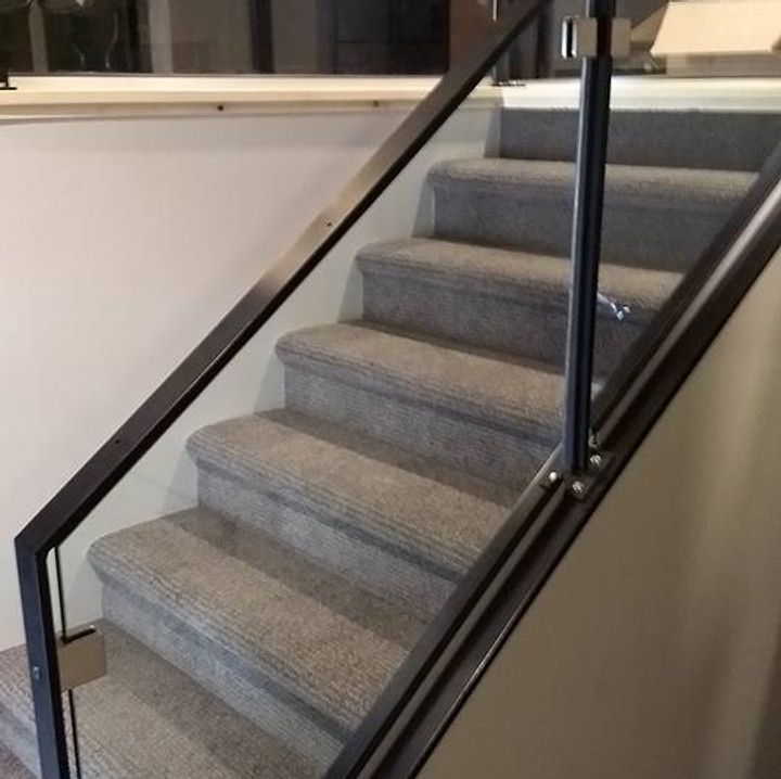 Staircase with gray carpet steps, glass railing, and dark metal frame.