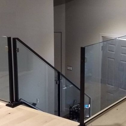 Glass railing with black frames on a wooden surface, leading to a staircase and doorway.