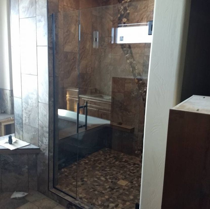 Glass shower enclosure with stone tile walls and pebble floor.