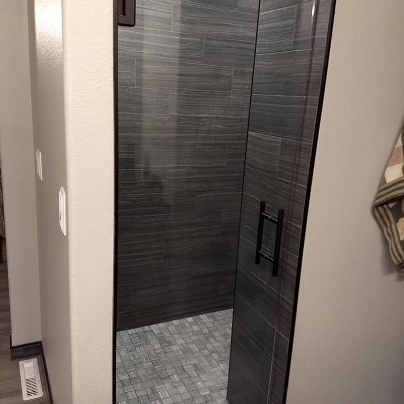 Gray tiled shower with glass door and black handle, visible from doorway.