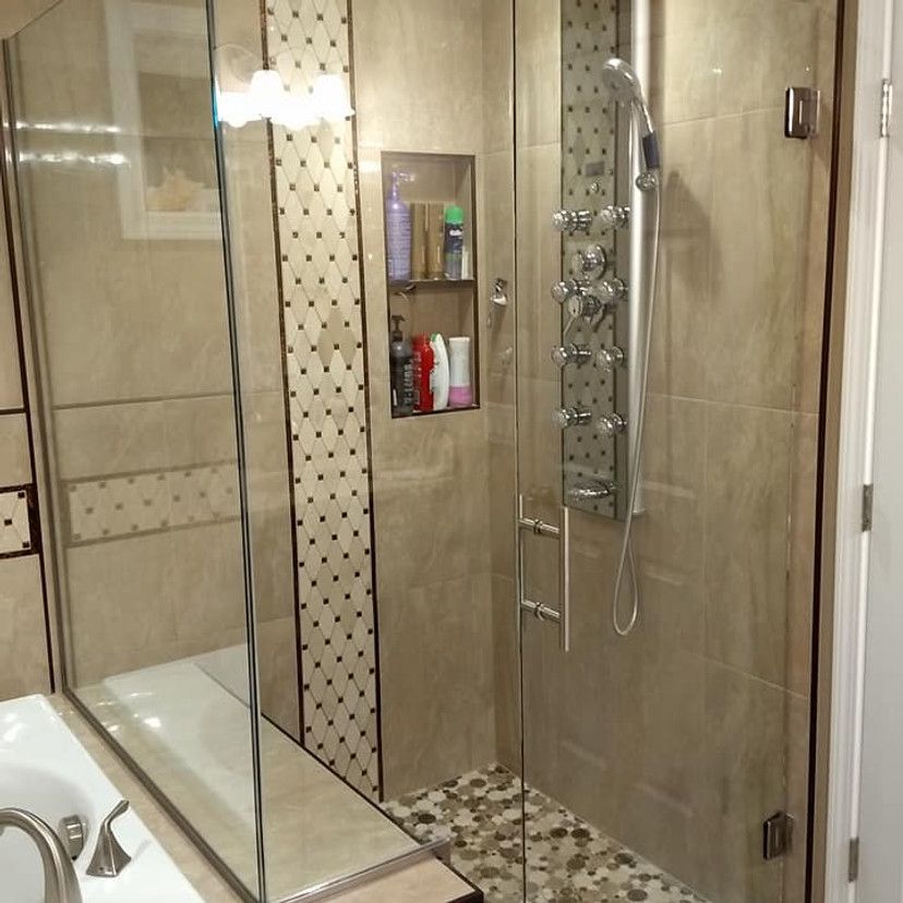 Modern shower with glass doors, stone tile floor, and built-in shelf holding toiletries.