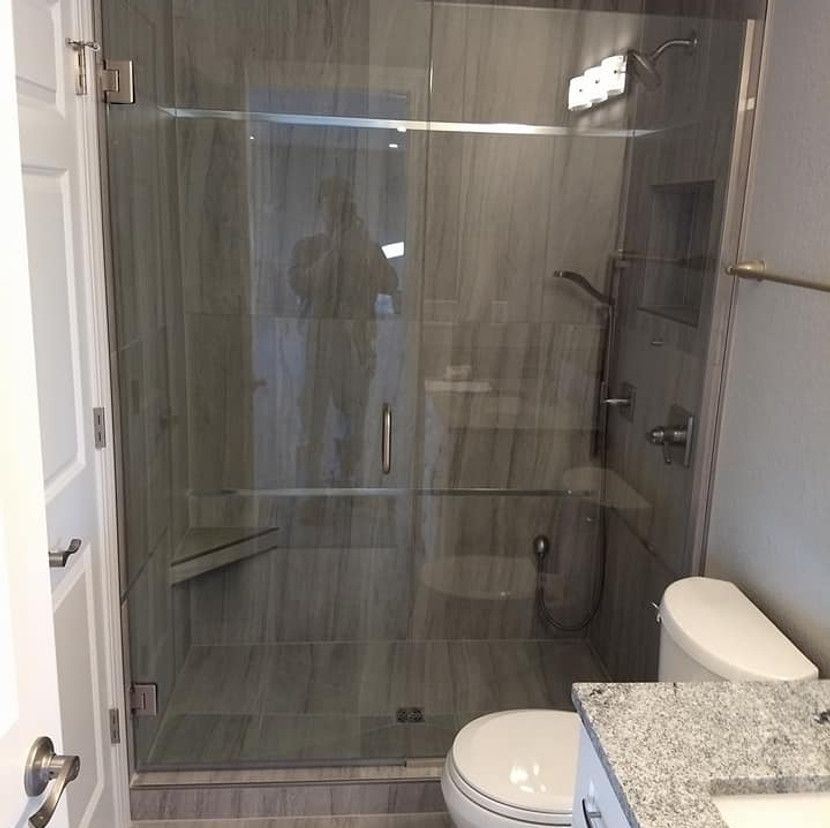 Glass shower stall with gray tiled walls, toilet, and vanity in a bathroom.