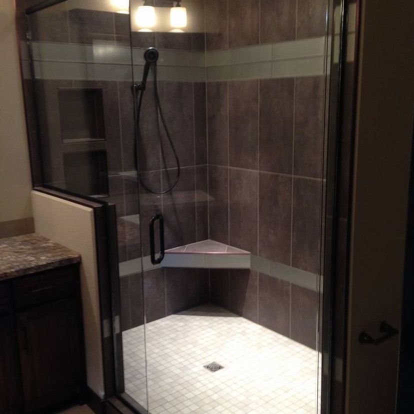 Corner shower with dark brown tiles, glass doors, built-in seat, and white tile floor.