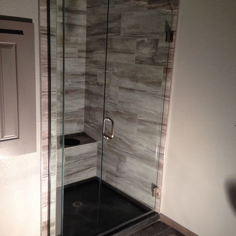 Glass shower with gray and brown tiled walls, black base, and a built-in shelf.
