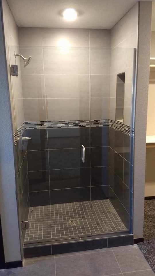 Shower with gray tiles, pebble floor, glass door, and recessed shelf.