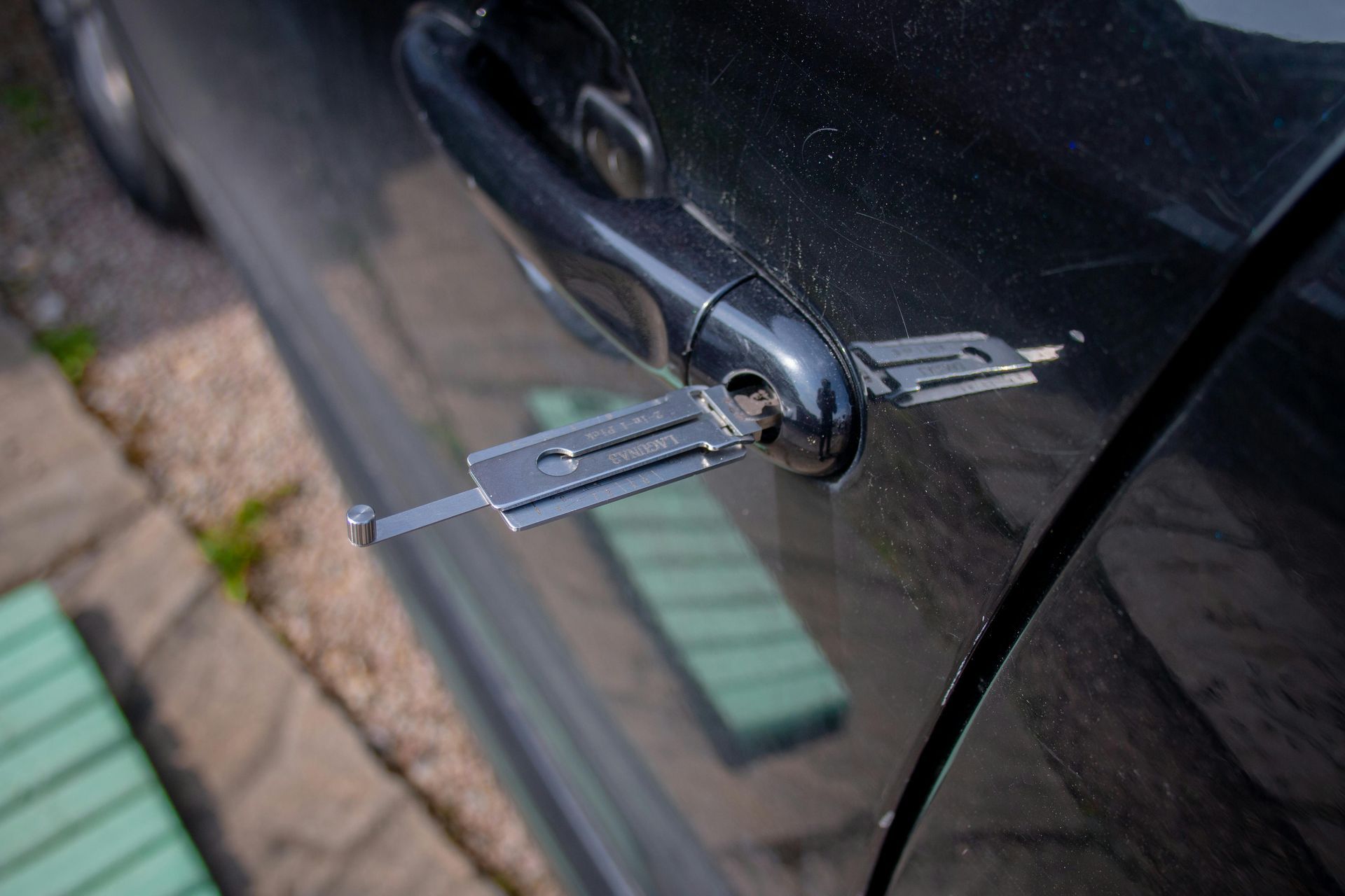 A car door being opened with a pick tool. Black car with the tool inserted in the door lock.