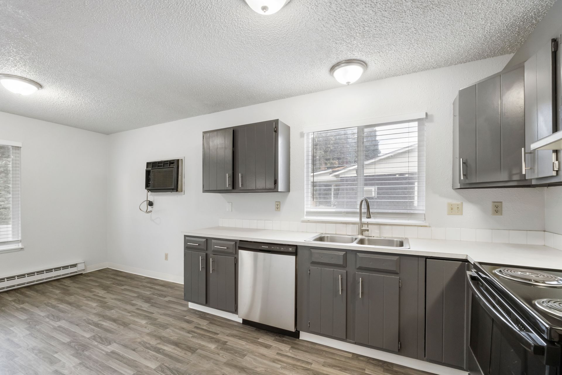 A kitchen with gray cabinets , stainless steel appliances , a sink , and a window.
