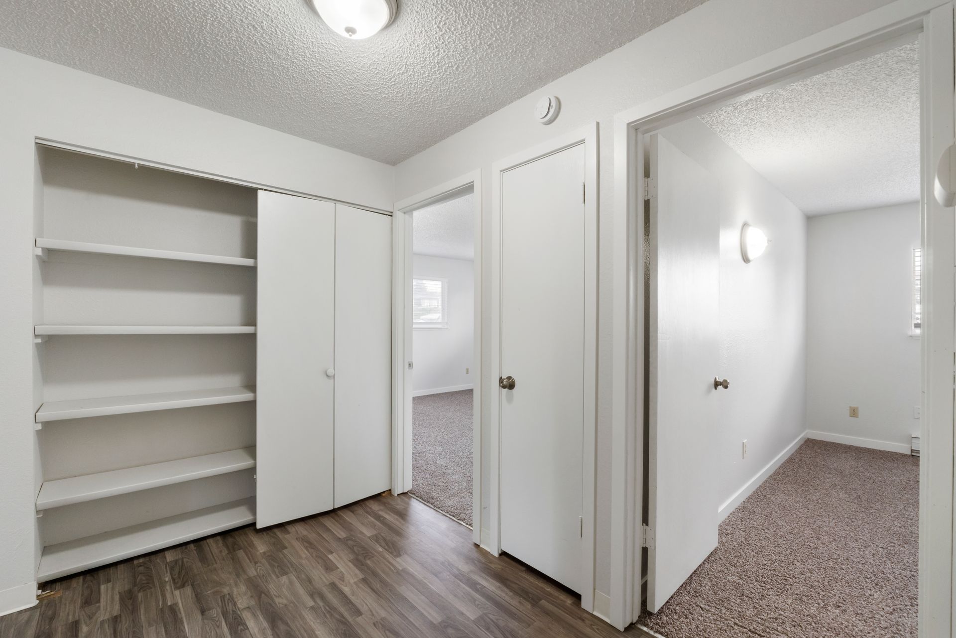 A hallway in a house with a closet and shelves.
