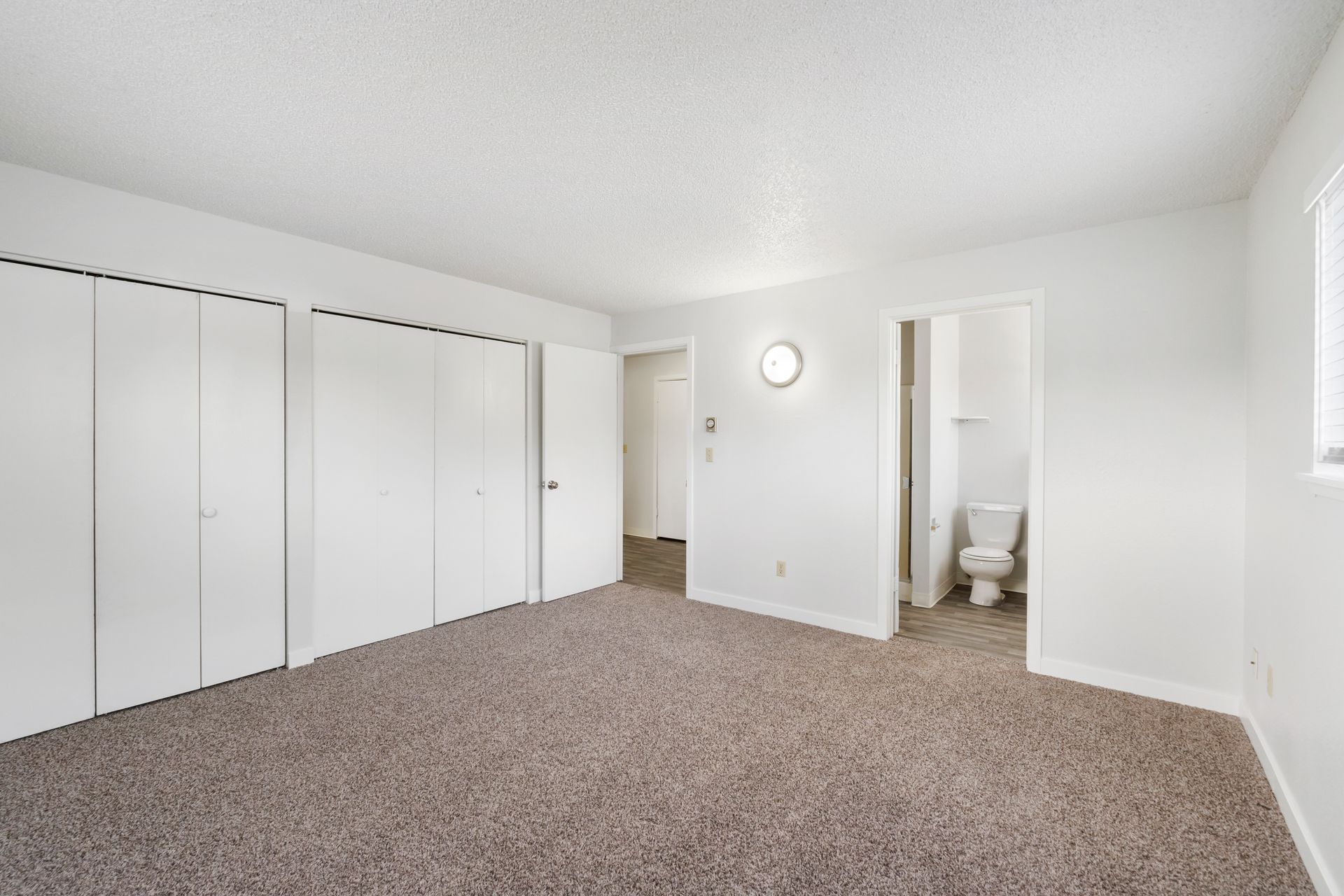 A bedroom with a carpeted floor , white walls and a toilet.