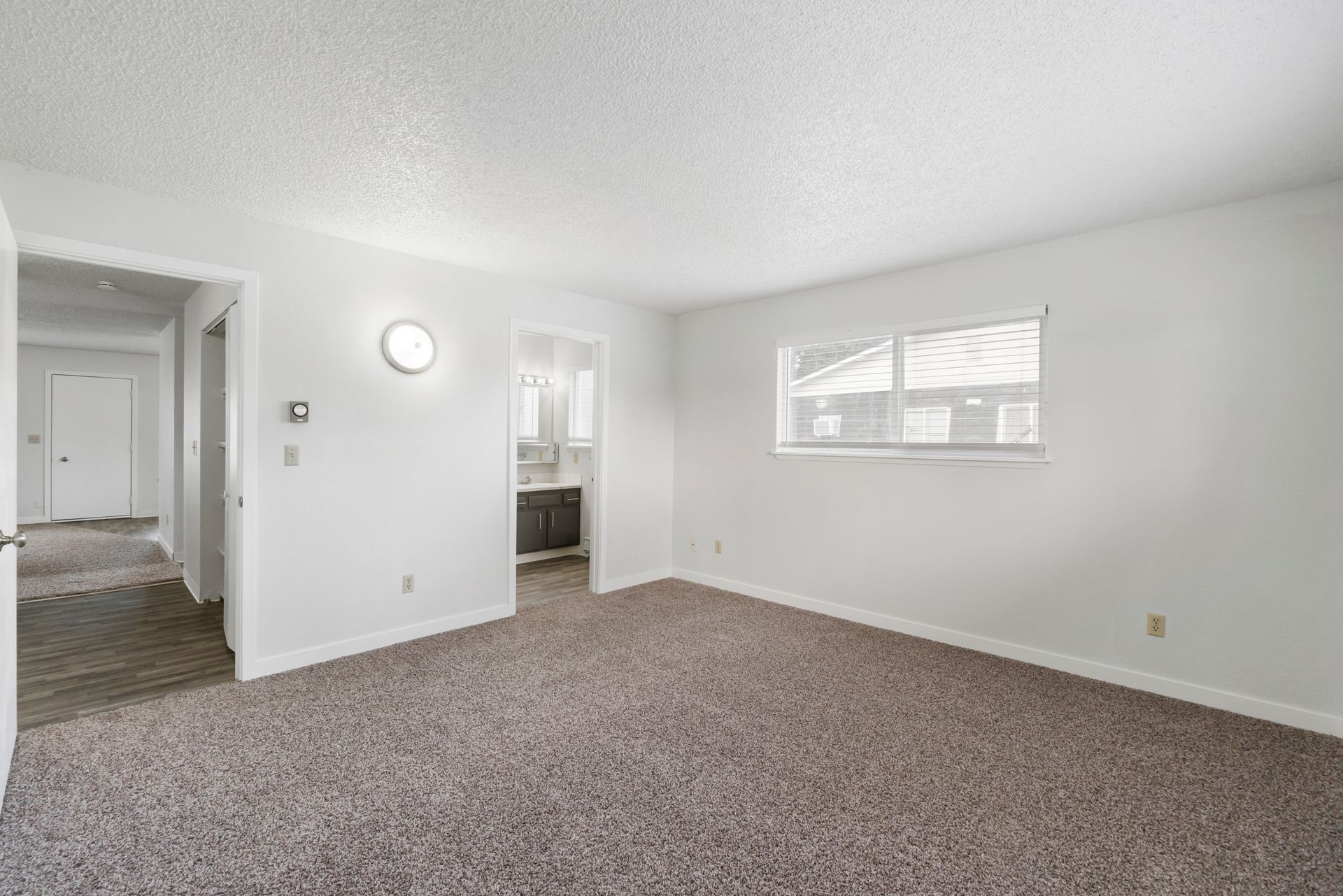 An empty living room with a carpeted floor and white walls.