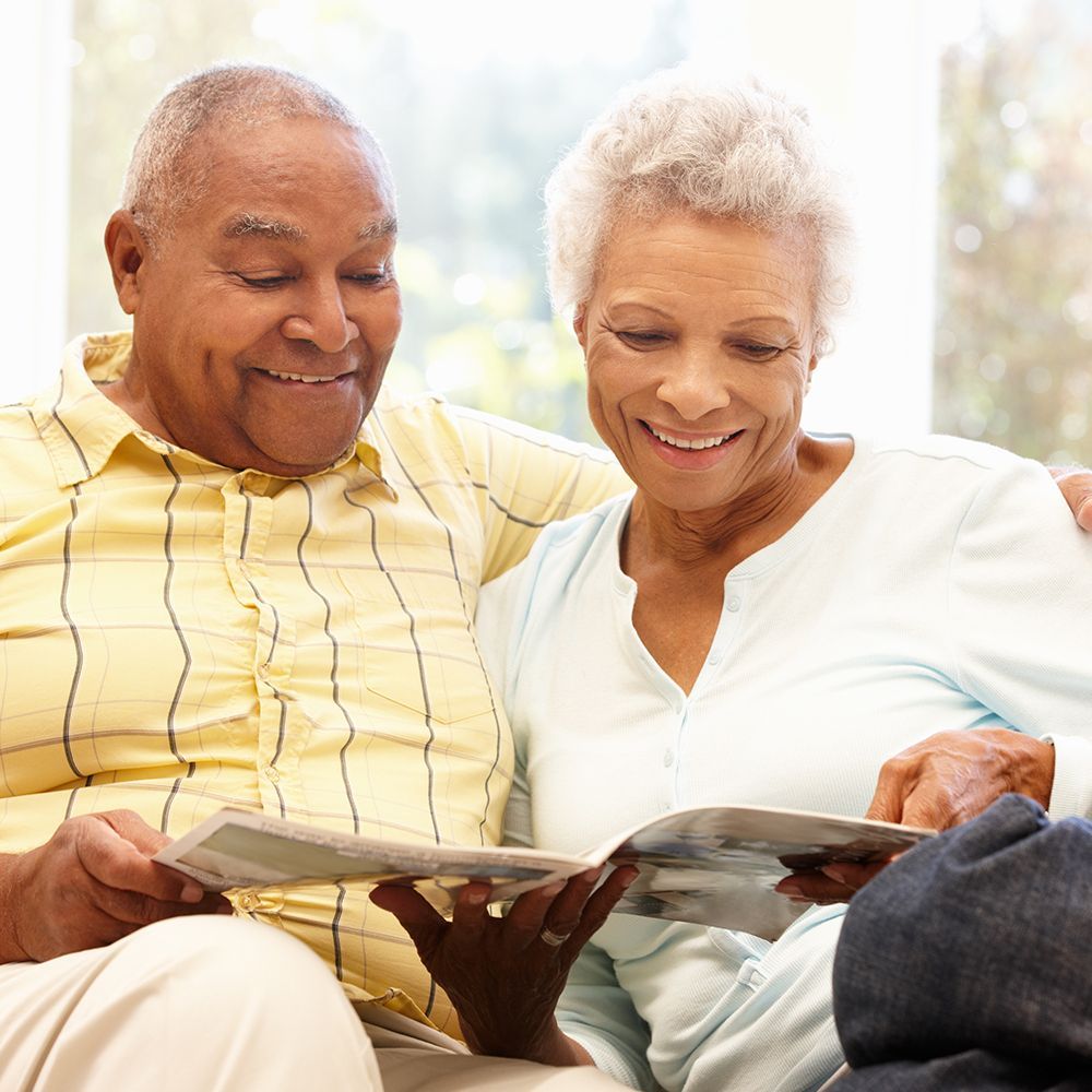 Two senior citizens on a couch reading a newsletter