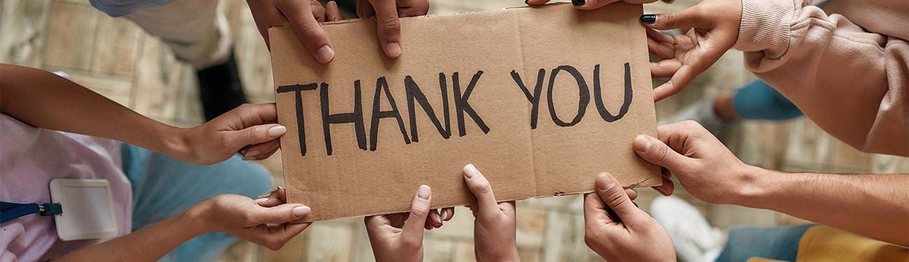 A group of people are holding a cardboard sign that says `` thank you ''.