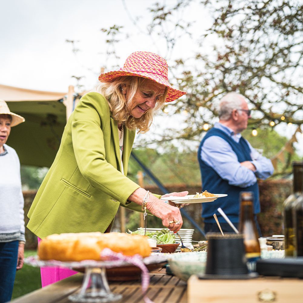 A lady with a pink hat on serving herself at an outdoor buffet table