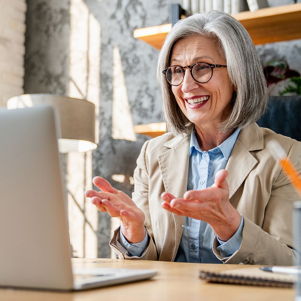 Smiling woman in glasses gestures during a laptop video call in a bright office