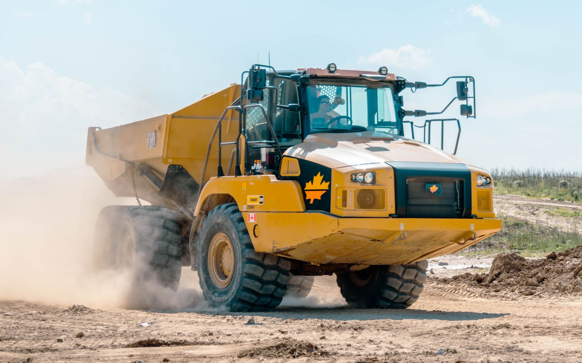 A yellow dump truck is driving through a muddy field.