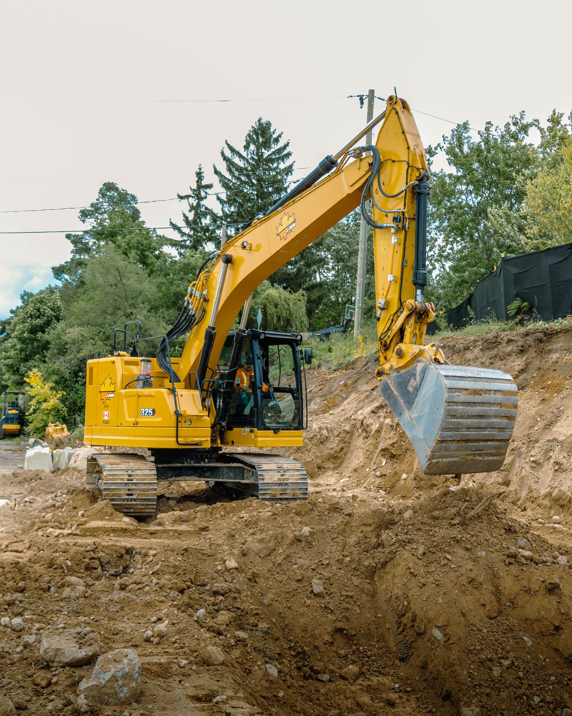 Yellow excavator digging in a dirt pit. Operator visible in the cab. Outdoors.