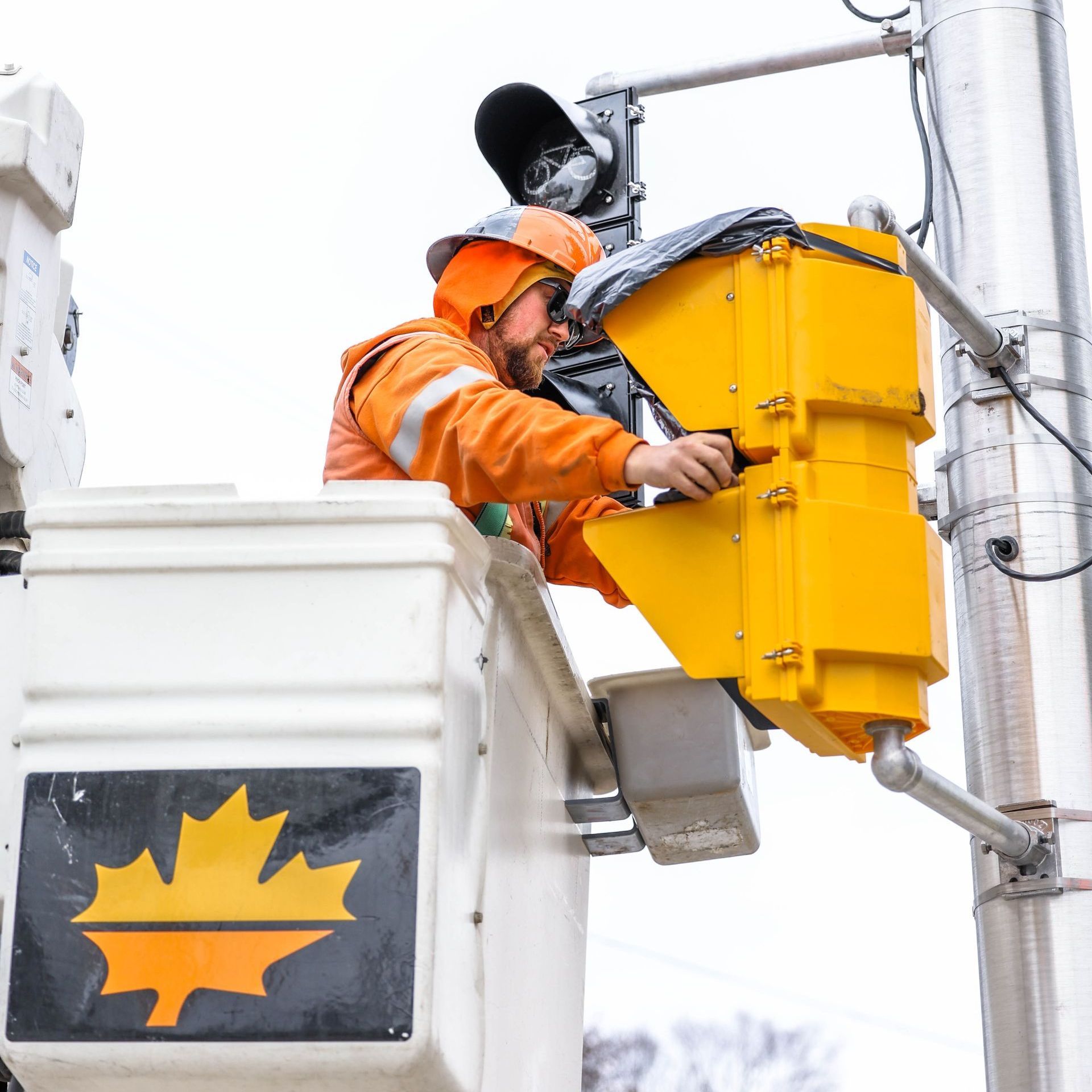 A man in an orange jacket is working on a traffic light