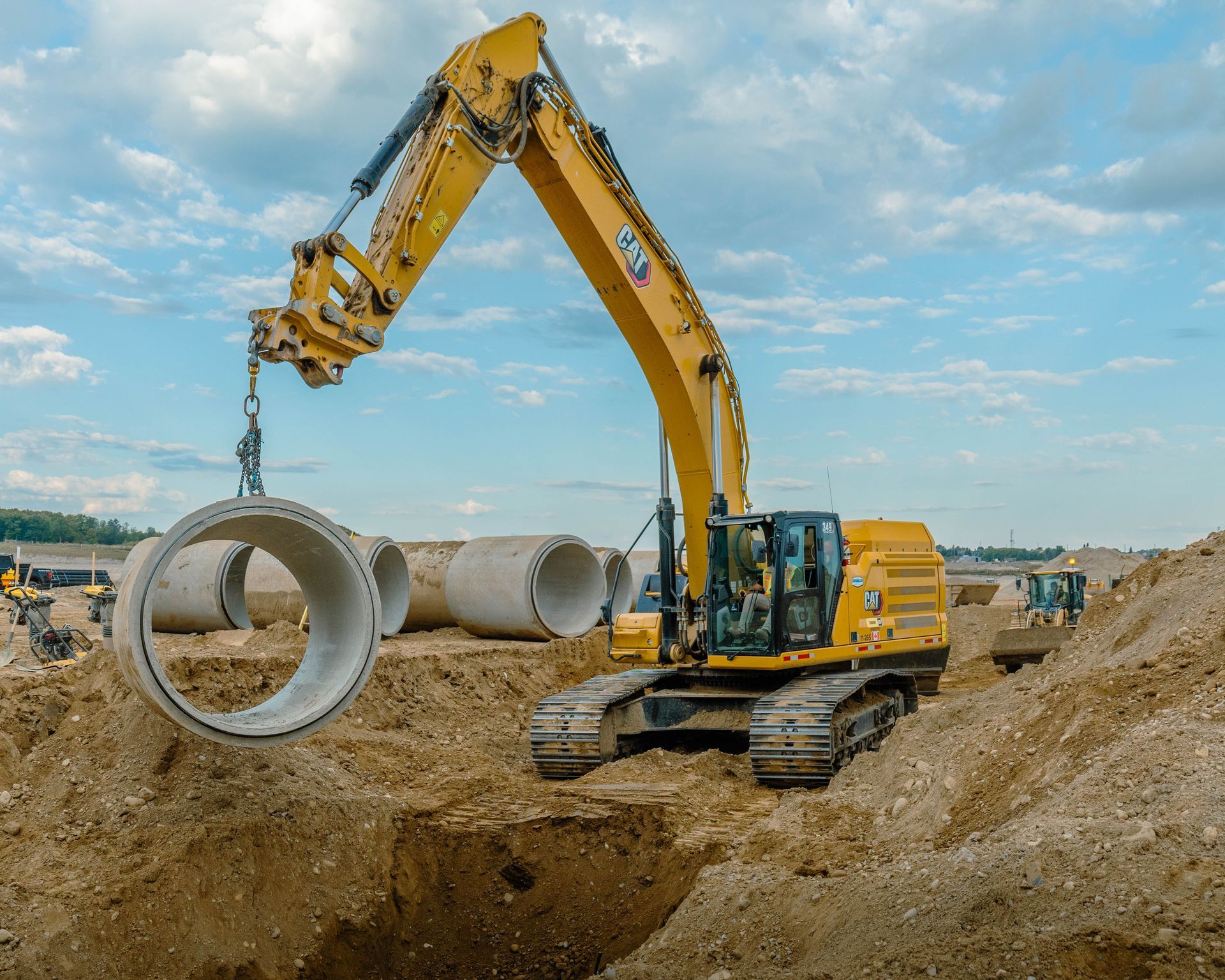 Yellow excavator lifting a concrete pipe at a construction site.
