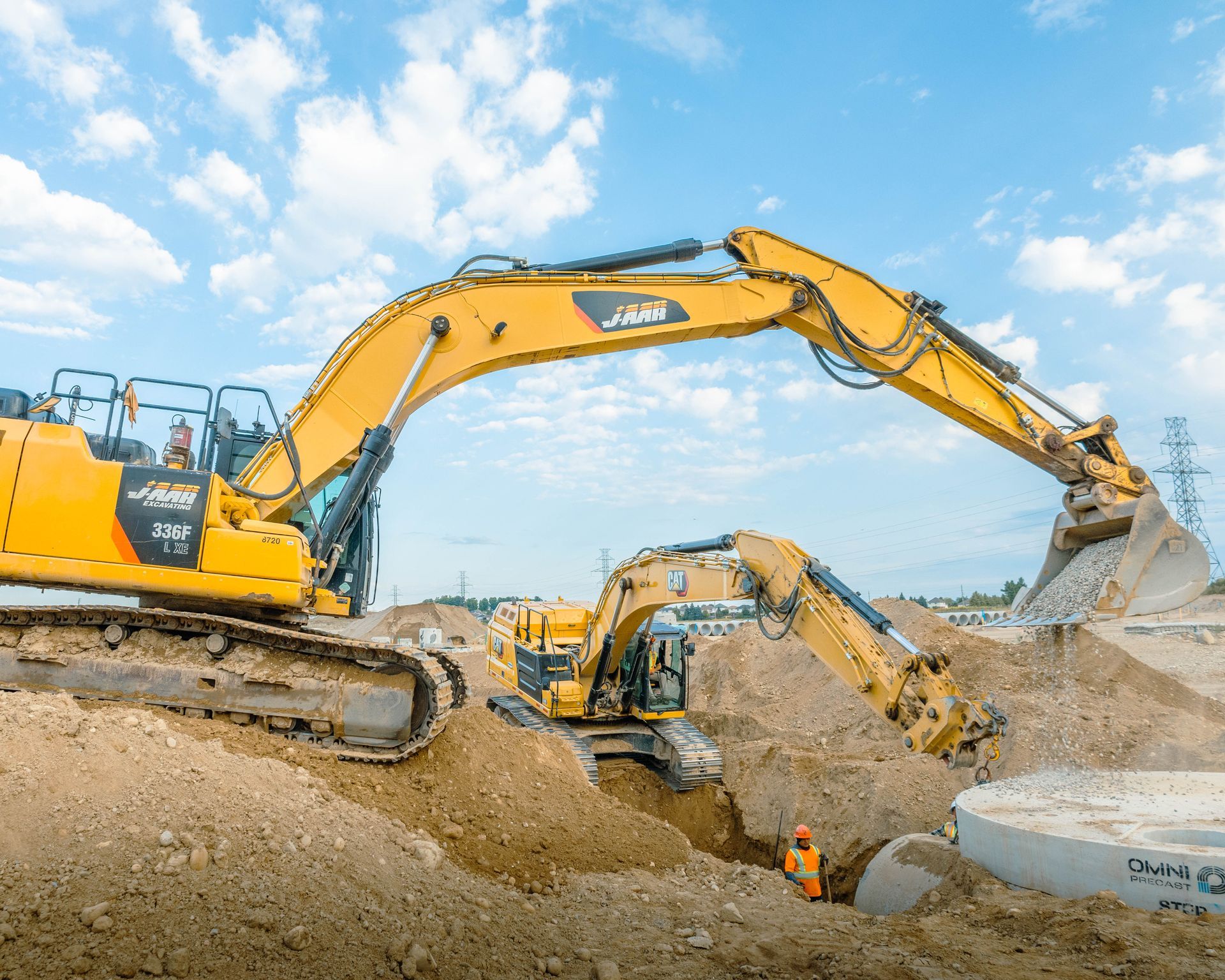 Two yellow excavators digging in dirt on a construction site under a blue sky.
