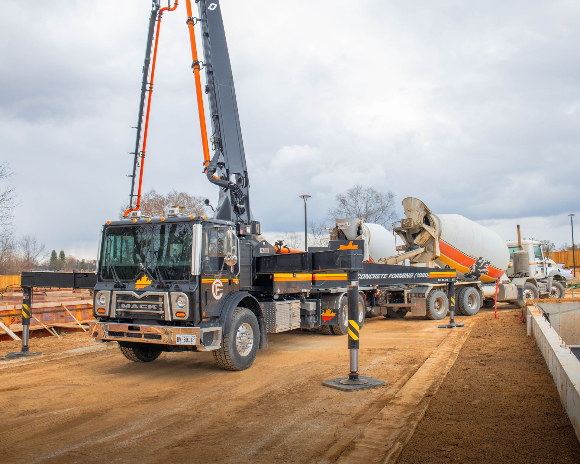 Concrete pump truck at construction site, boom extended. Cloudy sky, other trucks.