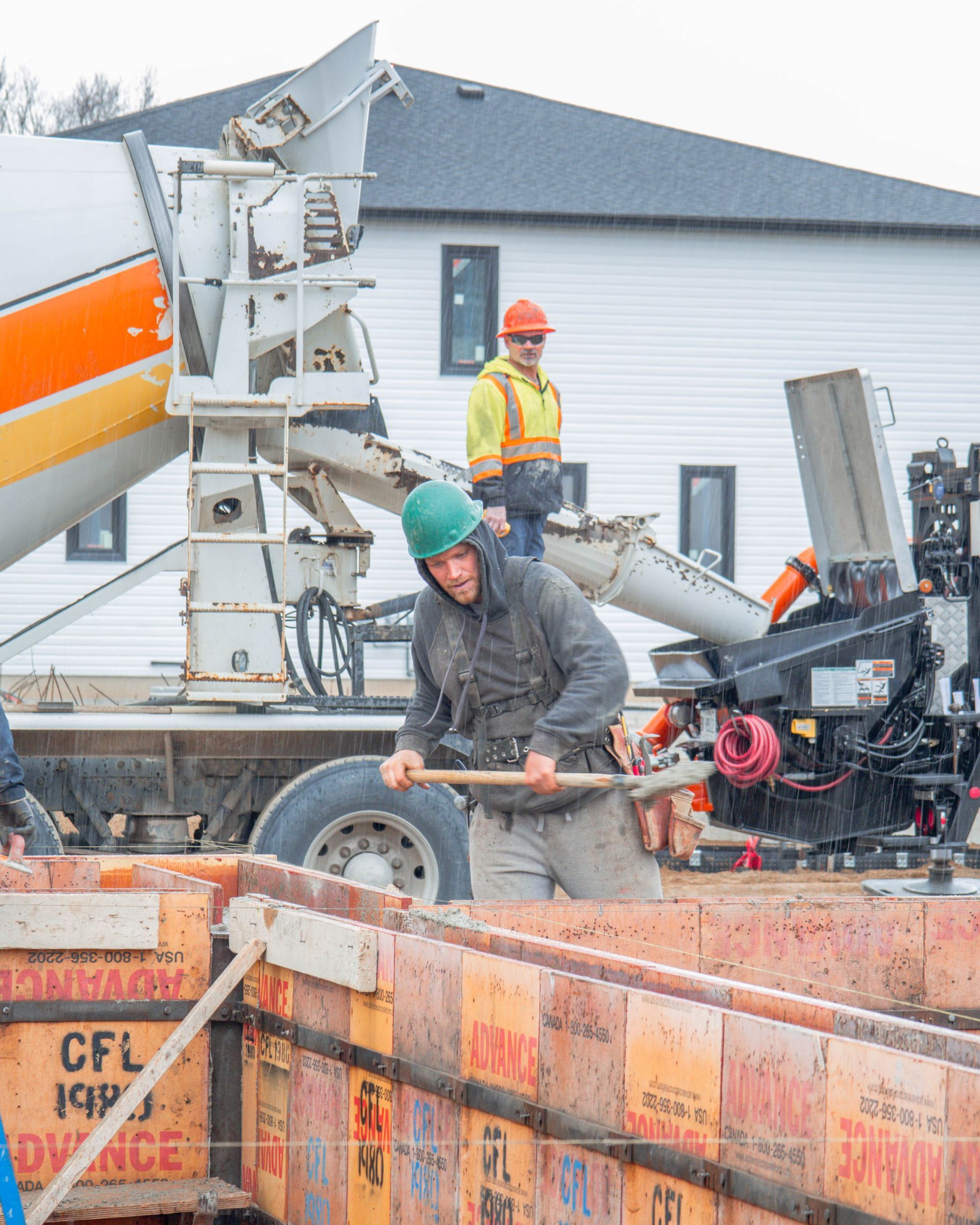 Construction workers pouring concrete from a truck into wooden forms at a building site.