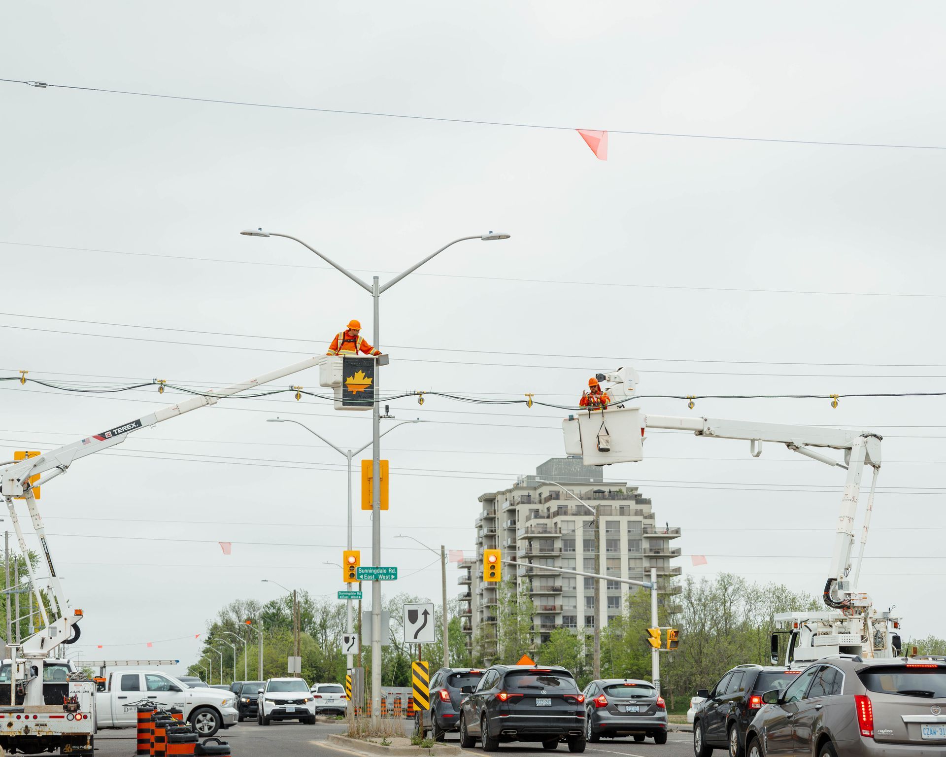 Utility workers in aerial lifts repair overhead wires at an intersection with stopped traffic.
